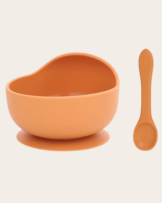 Orange bowl with suction cup and spoon on a beige background